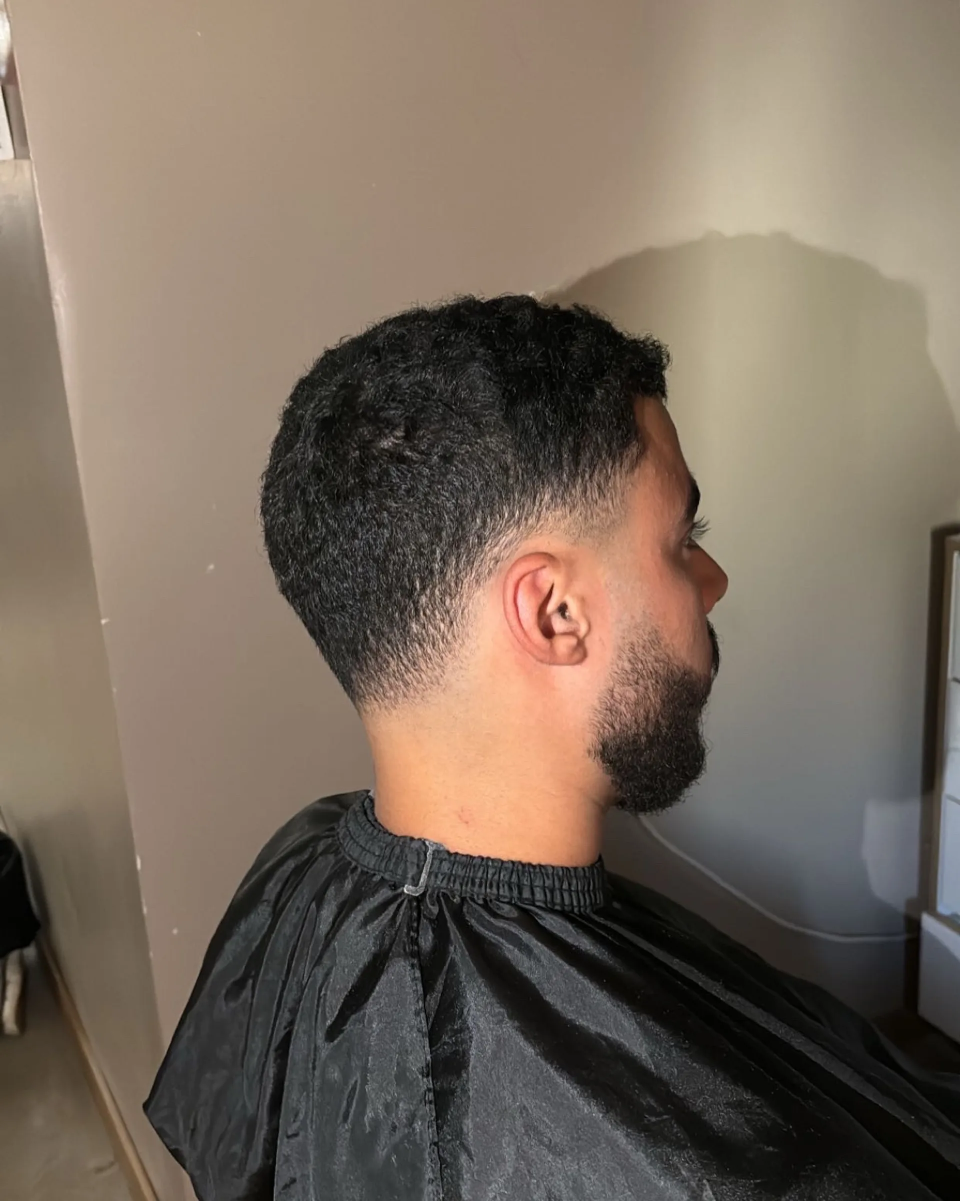 Taper fade die vanaf de nek naar boven opent, met een volle baard aan de kaaklijn.