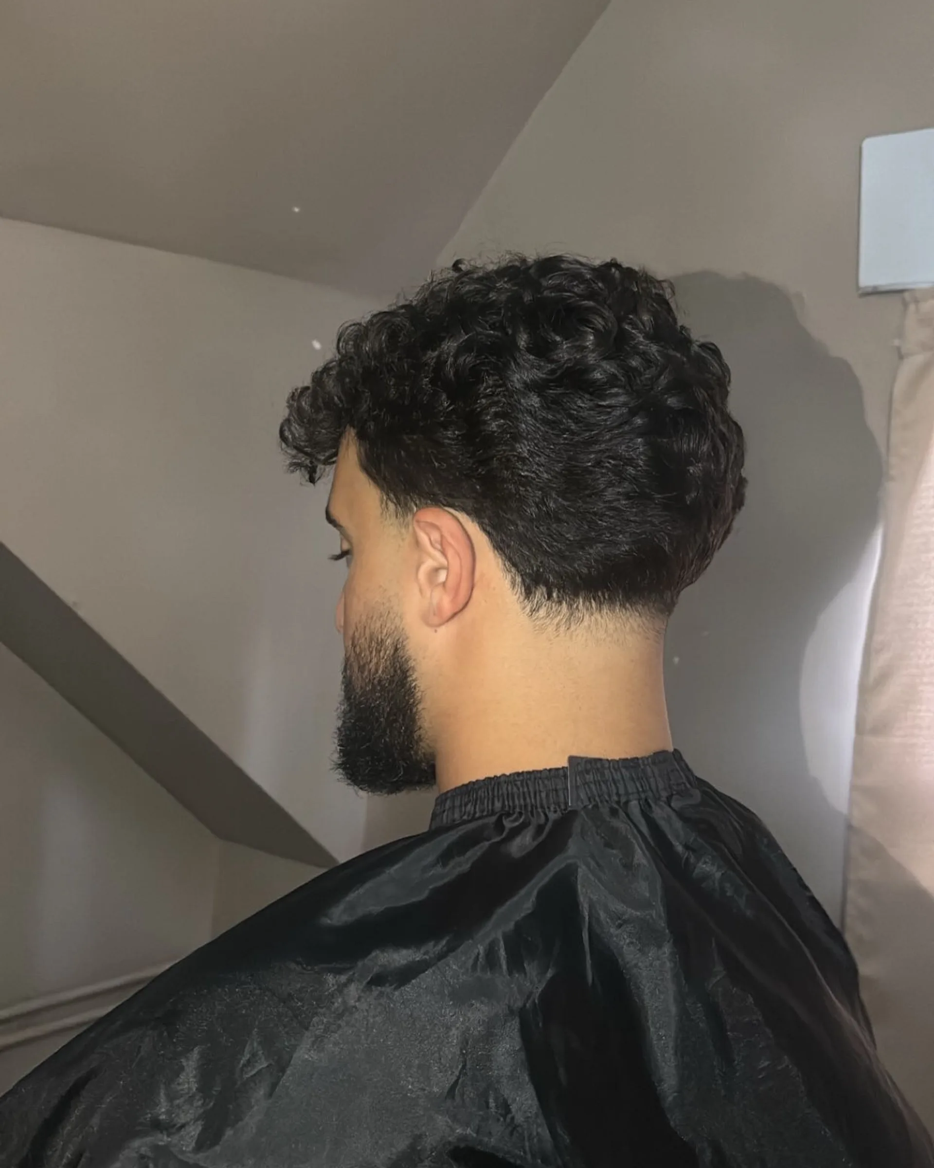 Achteraanzicht van krullend haar met een strak afgewerkte neklijn en een aansluitende baard.
